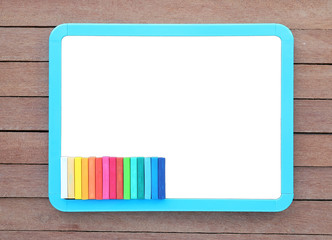 Blank white blackboard with colorful chalk on wooden plank.
