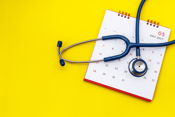 Blue stethoscope and white calendar on yellow background. Schedule to check heart or health check up concept