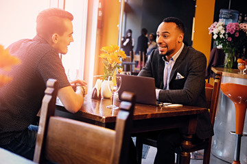 Two men talks and using a laptop in a restaurant.
