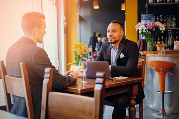 Two men talks and using a laptop in a restaurant.