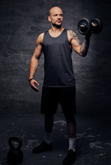 Sporty shaved head tattooed male doing shoulder workout with dumbbell.