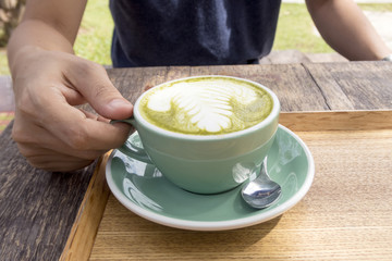 man holding a cup of hot green tea latte on wooden table.
