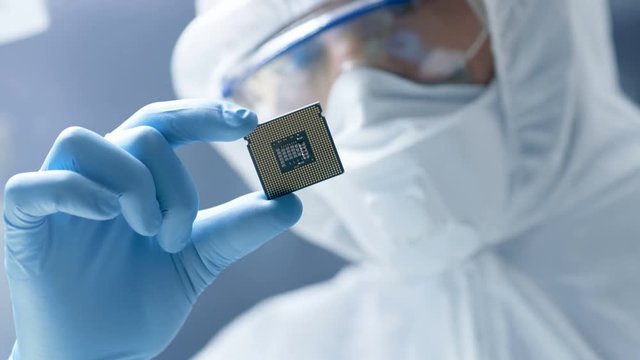 In Ultra Modern Electronic Manufacturing Factory Design Engineer in Sterile Coverall Holds Microchip with Gloves and Examines it. Shot on RED EPIC-W 8K Helium Cinema Camera.