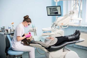Female dentist with dental tools - mirror and probe treating patient teeth at dental clinic office....