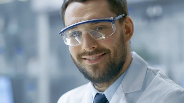 Handsome Research Scientist Wearing Safety Glasses Smiles into Camera.Shot on RED EPIC-W 8K Helium Cinema Camera.
