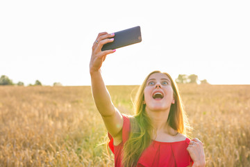 technology, summer holidays, vacation and people concept - funny young woman taking selfie by smartphone on cereal field