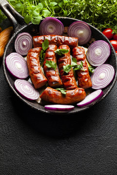 Grilled sausage, herbs and vegetables on black table