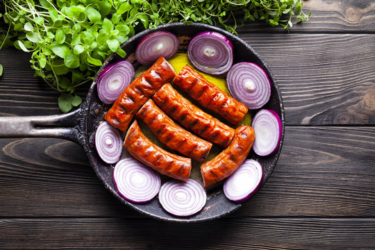Grilled sausage in a pan and fresh herbs on wooden table