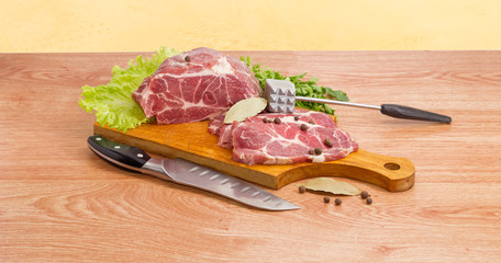 Pork neck on cutting board, meat tenderizer and kitchen knife