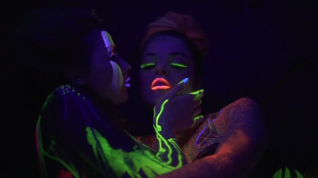 Closeup view of two beautiful girls in fluorescent clothing under UV black light petting each other. Homosexual relations between women. Same-sex couple