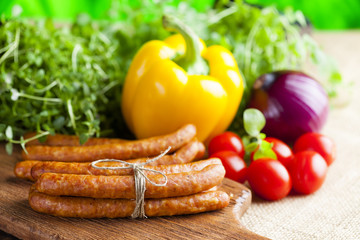 Sausage, herbs and vegetables on wooden and canvas background