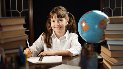 Eight years thoughtful school girl studying process, table place with books and globe, education concept