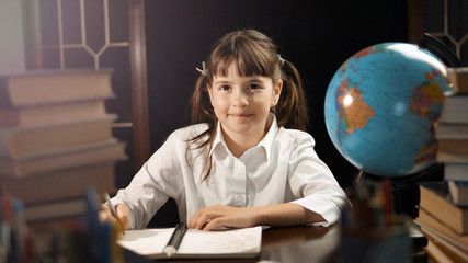 Eight years thoughtful school girl studying process, table place with books and globe, education concept