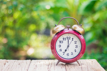 An antique red alarm clock on a wooden floor