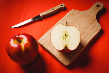 Red fresh apples chopped up on the old board on a red background