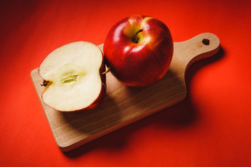 Red fresh apples chopped up on the old board on a red background