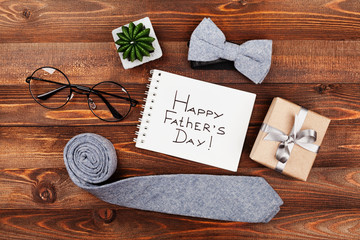 Happy Fathers Day background with notebook, gift, glasses, necktie and bowtie on wooden rustic table top view in flat lay style.
