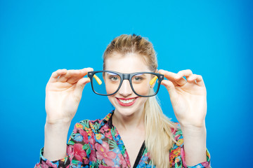 Portrait of Funny Blonde Woman with Ponytail Wearing Colorful Shirt and Fashionable Eyeglasses on Blue Background. Sensual Cute Girl is Posing in Studio.