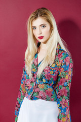 Portrait of Sensual Blonde Model with Long Hair in Colorful Shirt and White Skirt is Looking at the Camera on Pink Background. Pretty Cute Girl is Posing in Studio.