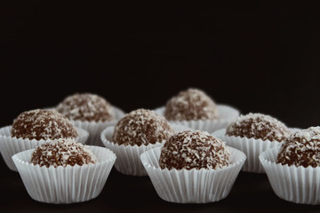 Coconut and chocolate balls in white paper cupcakes  on black background.