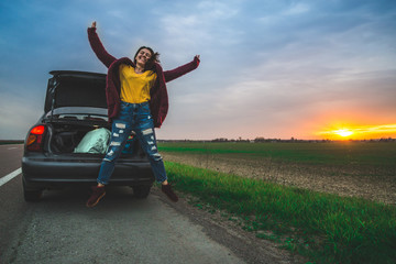 Teenage girl jumping on open road near car