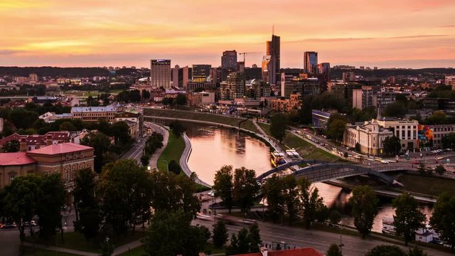 Aerial view of Vilnius, Lithuania at sunset. Modern city with many skyscrapers and car traffic lights, river. Time-lapse of colorful sunset sky