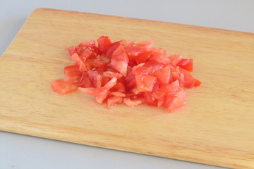 Step by step cooking. Freshchopped tomato on a wooden cutting board on a grey background