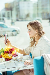 Smiling girl makes a selfie sitting on the terrace of cafe