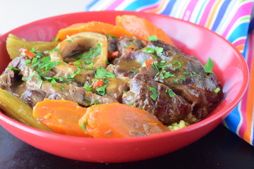 Italian traditional veal dish osso buco with cooked carrots, potato, cellery in a red ceramic bowl
