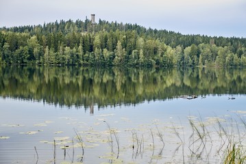 Summer landscape at Aulanko nature park in Finland. Reflection of the scene and the lookout tower in the still water of the lake.