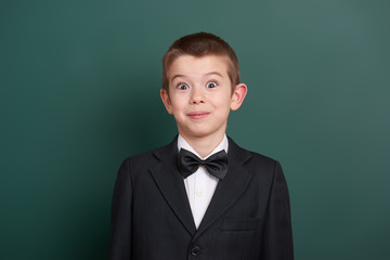 surpised school boy portrait near green blank chalkboard background, dressed in classic black suit, one pupil, education concept