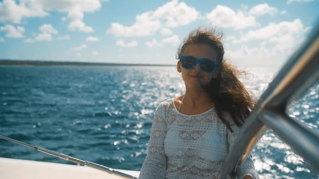 4k UHD. Young pretty beautiful girl in sunglasses sitting on the edge of the yacht among the blue amazing caribbean sea. Saona island. teal and orange style. Smile happiness. Brownhair. Sunny, sunrise