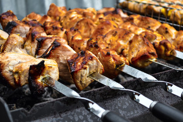 Grilled kebab cooking on metal skewer closeup. Roasted meat cooked at barbecue. Traditional eastern dish, shish kebab. Grill on charcoal and flame, picnic