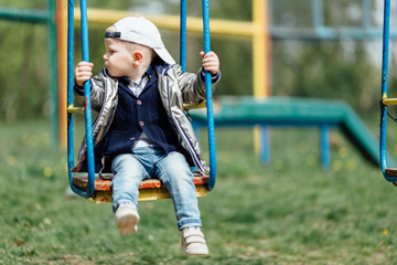 Little boy riding a swing in park playground