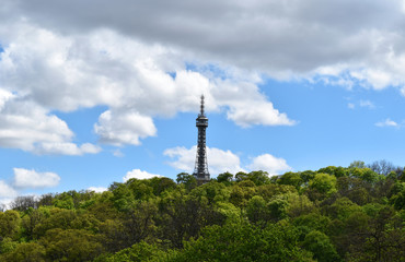 Fototapeta premium A metal tower in a green forest with blue sky and white clouds.
