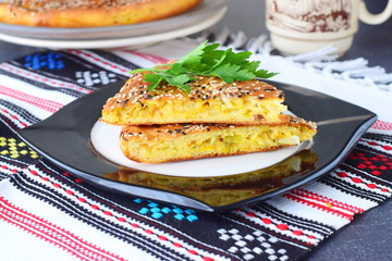 Two pieces of white cabbage pie with carrot on a black plate with cup of tea and the rest of the pie on a textile background. Healthy breakfast. Simple backing. Healthy eating concept