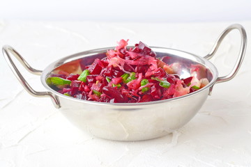 Mix of boiled beetroot, beans, sauerkraut, pickles and green onion with olive oil and wine vinegar in a metal plate with hands on a white background. Fastening. Healthy food. Healthy eating concept