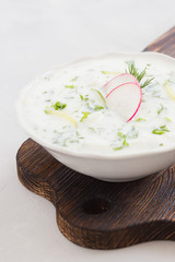 Yoghurt cold soup with radish, cucumber and dill on wooden board. Traditional soup tarator with radish and cucumber. Cold summer soup - okroshka. Healthy eating. Clean eating