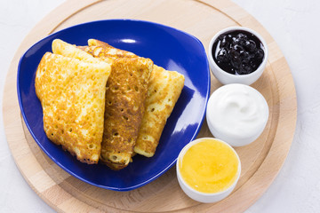 Crepes with jam, honey and sour cream on a blue plate on wooden board. Pancakes with honey,jam and sour cream on a plue plate.