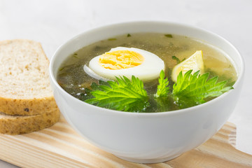 Nettle soup with vegetables and lemon in a white bowl on wooden board. Summer dishes. Light summer soup. Healthy vegetarian soup.