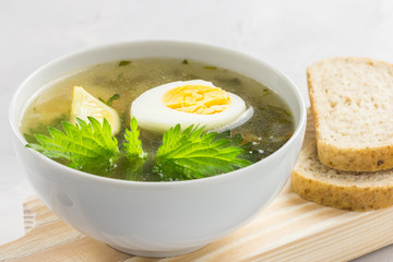 Nettle soup with vegetables and lemon in a white bowl on wooden board. Summer dishes. Light summer soup. Healthy vegetarian soup.