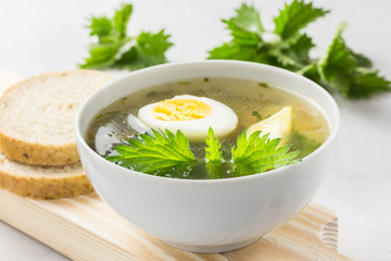 Nettle soup with vegetables and lemon in a white bowl on wooden board. Summer dishes. Light summer soup. Healthy vegetarian soup.