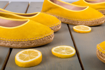 Yellow espadrilles shoes near slices of lemon on wooden background. Close up.