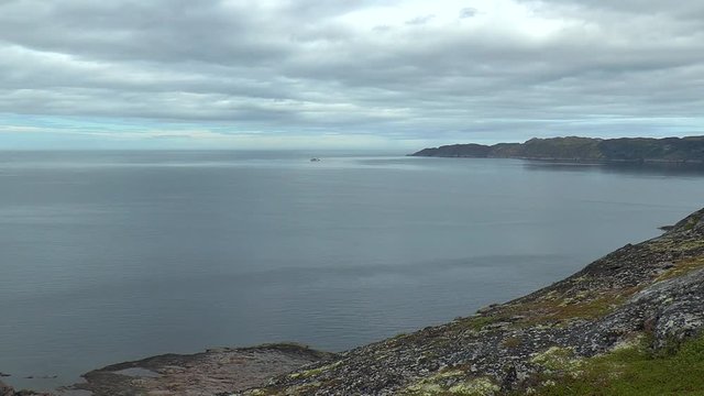 The harsh Northern landscape - rocks, calm, cold sea and a small ship in the distance under 
low cloudy sky.  Summer day.