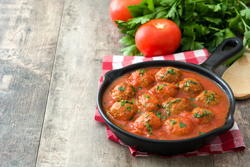 Meatballs with tomato sauce in iron frying pan on wooden table