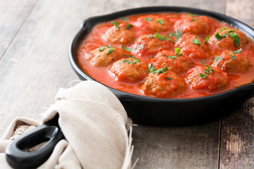Meatballs with tomato sauce in iron frying pan on wooden table