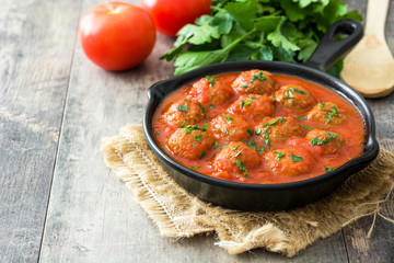 Meatballs with tomato sauce in iron frying pan on wooden table