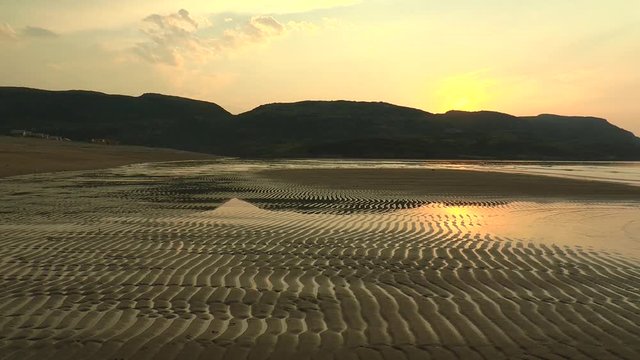 Severe northern landscape - a sandy shore at low tide 

against the backdrop of low mountains and a  hamlet in the 

distance. Summer windless evening.
