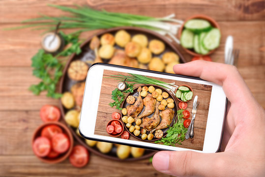 Hands taking photo chicken legs with baked potatoes and vegetables  with smartphone.