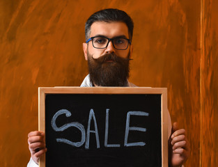 Bearded man, brutal caucasian hipster holding sale inscription on blackboard